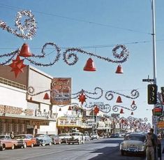 a street with cars parked on the side of it and christmas decorations hanging from the buildings