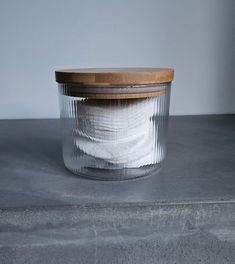 an empty glass jar with white cloth inside on a gray countertop next to a wooden lid