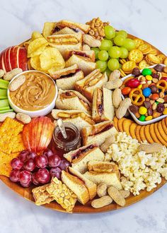 a platter filled with crackers, grapes, apples, nuts and other snacks