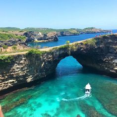 a boat traveling through the water near an arch shaped rock bridge over clear blue water