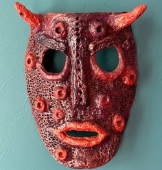 a red mask hanging on the wall with holes in it's face and eyes