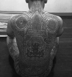 a man sitting on the floor with his back turned to the camera and tattoos all over his body