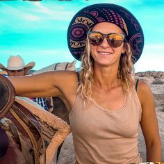 a woman wearing a cowboy hat and sunglasses standing next to a horse