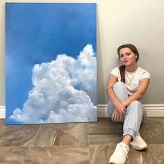 a woman sitting on the floor next to a painting