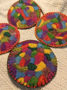 four multicolored coasters on a white tablecloth with crocheted designs