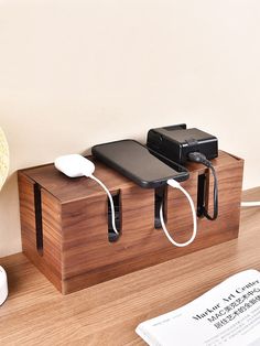 two cell phones are plugged in and charging on a wooden stand next to a lamp