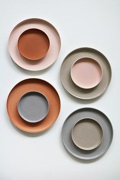 four plates with different colors and shapes on white table top, one is orange the other two are gray