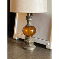 a glass lamp sitting on top of a wooden table next to a white wall and floor