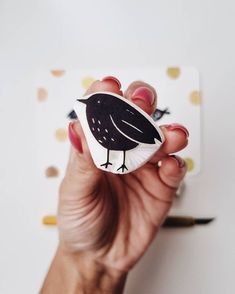 a hand holding a sticker with a black and white bird on it's side