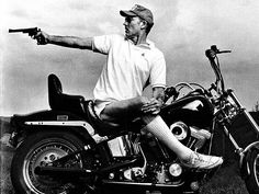 a man sitting on top of a motorcycle pointing at the sky with his hand out