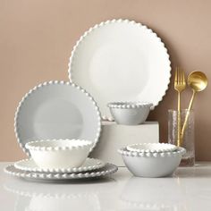 white dishes with scalloped rims and gold spoons are displayed on a table