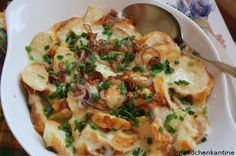 a white bowl filled with pasta covered in cheese and green onions next to a spoon