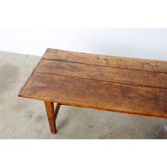 an old wooden table sitting on top of a cement floor next to a white wall