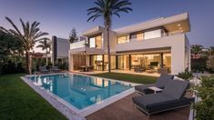 a house with a swimming pool and lounge chairs in front of it at night time