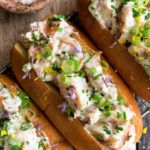 three hot dogs with toppings sitting on top of a cutting board