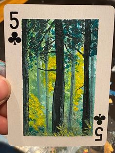 a person holding up a playing card with trees in the woods on it's side