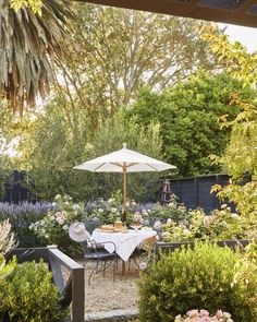 an outdoor dining area with table, chairs and umbrella in the middle of it surrounded by flowers