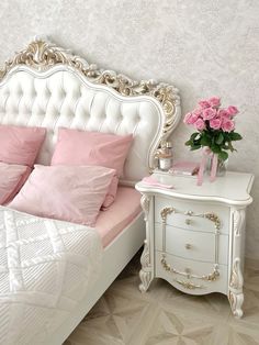 a white bed sitting next to a pink flower vase on top of a dresser in a bedroom