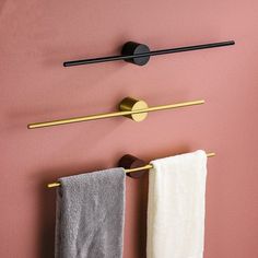 two towels hanging on the wall next to a towel rack and toilet paper roll in front of a pink wall