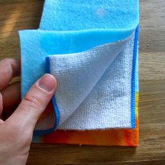 a hand is holding two cloths on top of a wooden table with a blue and white towel