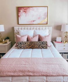 a white bed topped with pink pillows next to two nightstands and a painting on the wall