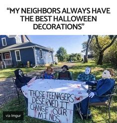 three people sitting at a table in front of a sign that says, my neighbors always have the best halloween decorations