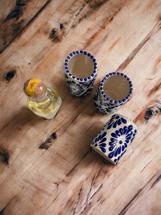 three blue and white cups sitting on top of a wooden table next to a bottle