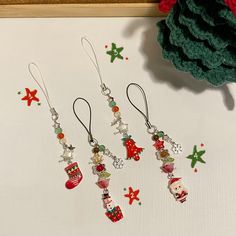 three christmas themed earrings hanging from hooks on a table next to a potted plant