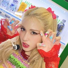 a woman with long blonde hair holding her hands up in front of her face and wearing colorful nail polish