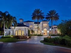 a large white house with palm trees in the front yard and driveway at night time