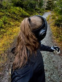 a woman with headphones on walking down a dirt road in the woods and trees