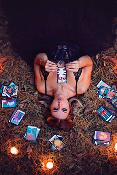 a woman laying on the ground surrounded by candles and playing cards with her eyes closed