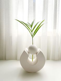 a white vase with a plant in it sitting on a table next to a window