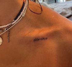 a woman's back with the word divine written on her left shoulder and two bracelets attached to it