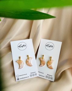 two small earrings with gold colored details are on a white card next to a green plant