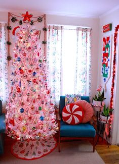 a pink christmas tree in the corner of a room with blue chairs and candy canes