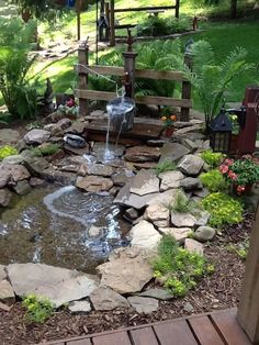 a small pond in the middle of a garden with rocks and water flowing from it