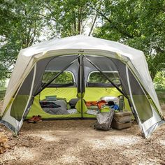 a tent is set up in the woods with its doors open and camping equipment inside