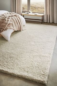 a bedroom with a large white rug on the floor and a bed in front of a window