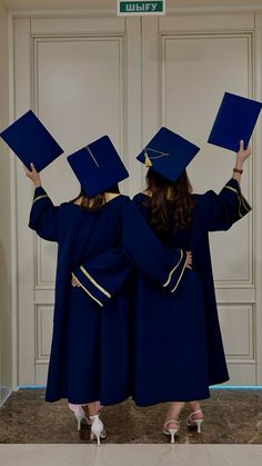 two women in graduation gowns are holding up their caps