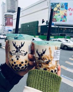 two people holding up coffee cups in front of a city street with cars on it