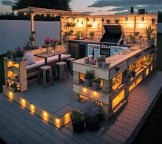 an outdoor kitchen is lit up with lights and potted plants on the outside deck