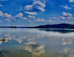 the sky is reflected in the still water on the lake's surface, while clouds and trees are visible in the distance