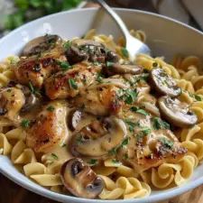 a bowl filled with pasta and mushrooms on top of a wooden table next to a fork