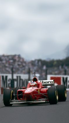 a man driving a red race car down a track with spectators in the background on a cloudy day