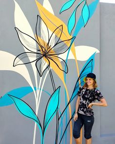 a woman standing in front of a painted flower on the side of a gray building