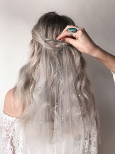 a woman with long grey hair wearing a veil over her head and combing it's hair