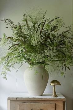 a vase filled with lots of green plants on top of a wooden table next to a mushroom