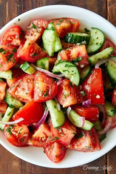 a white bowl filled with cucumber, tomato and onion salad on top of a wooden table