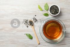 a cup of green tea next to a spoon and some leaves on a white wooden table